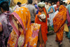 A woman in a vibrant orange sari at a bustling market in Delhi, India, 2014, surrounded by rich textures and colors of everyday life.