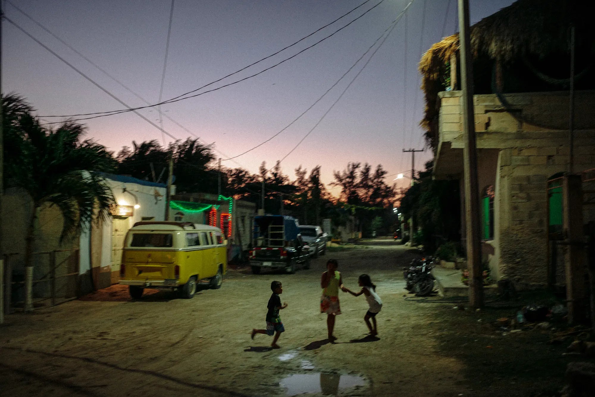 Children playing under the glow of streetlights in El Cuyo, Mexico, while the sky blends into warm night hues, 2019.